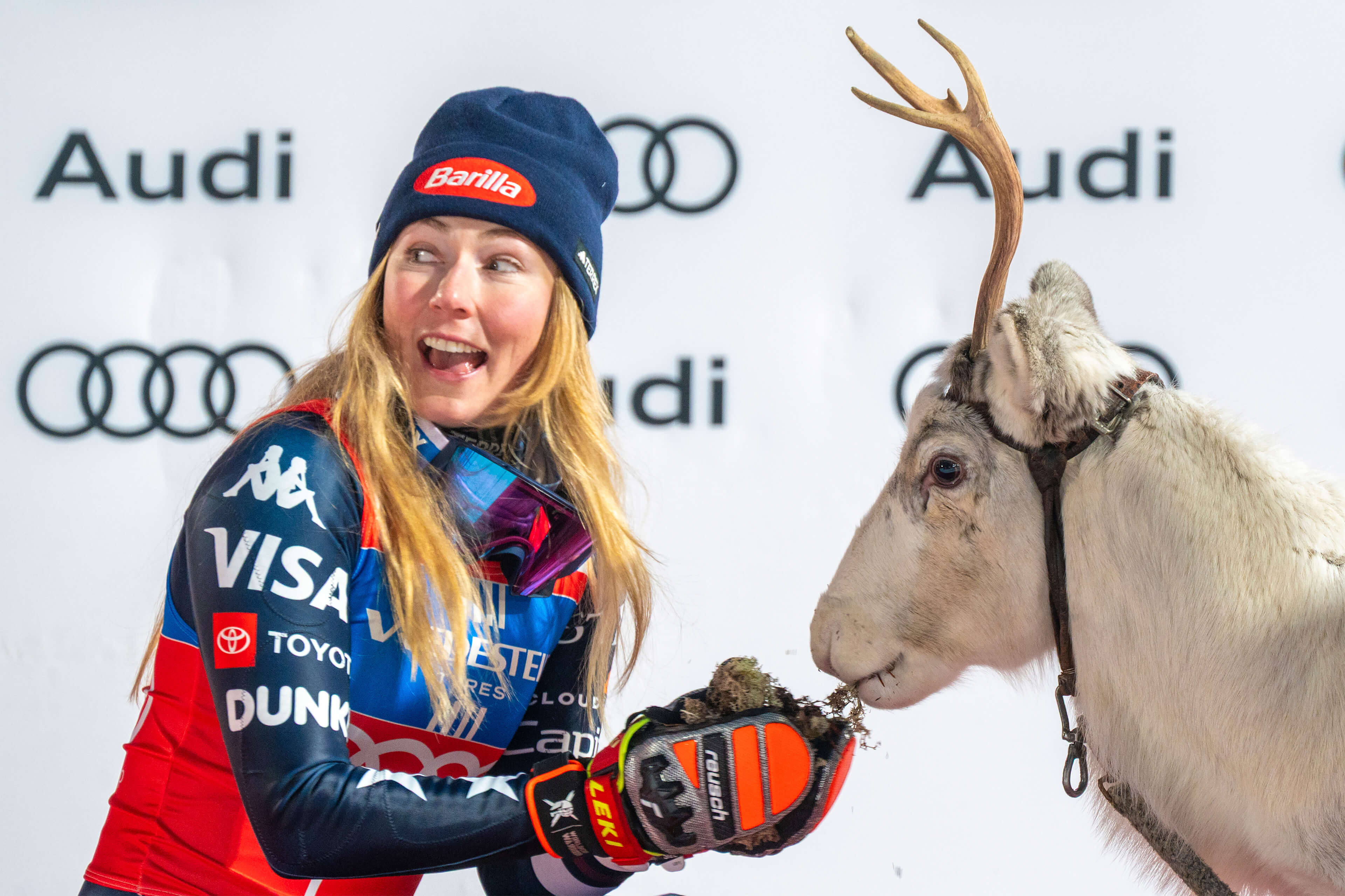 Mikaela Shiffrin syöttää nauraen palkintoporoaan Levin alppihiihdon maailmancupin palkintokorokkeella.